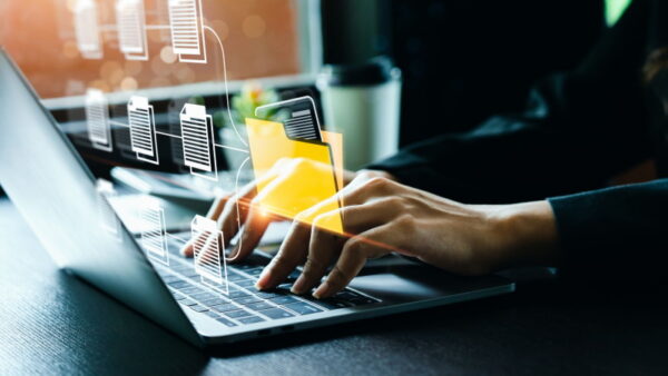 Pessoa a digitar num portátil com gráficos sobrepostos que simulam a organização e a transferência de ficheiros digitais para uma pasta amarela flutuante.